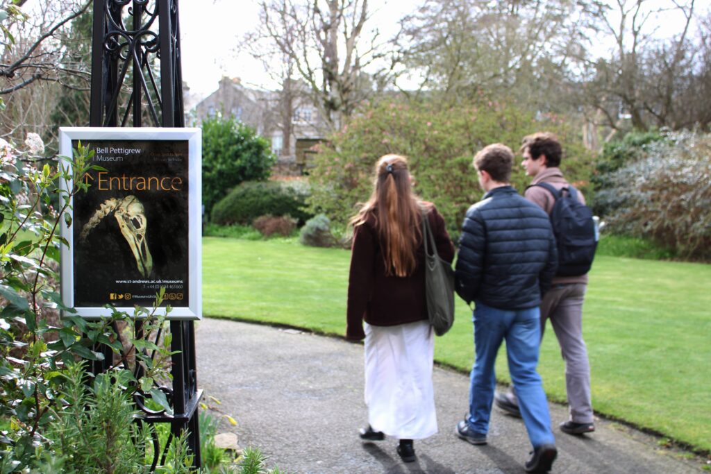 Students walking in a garden. Sign on the side says 'Bell Pettigrew Museum Entrance'.